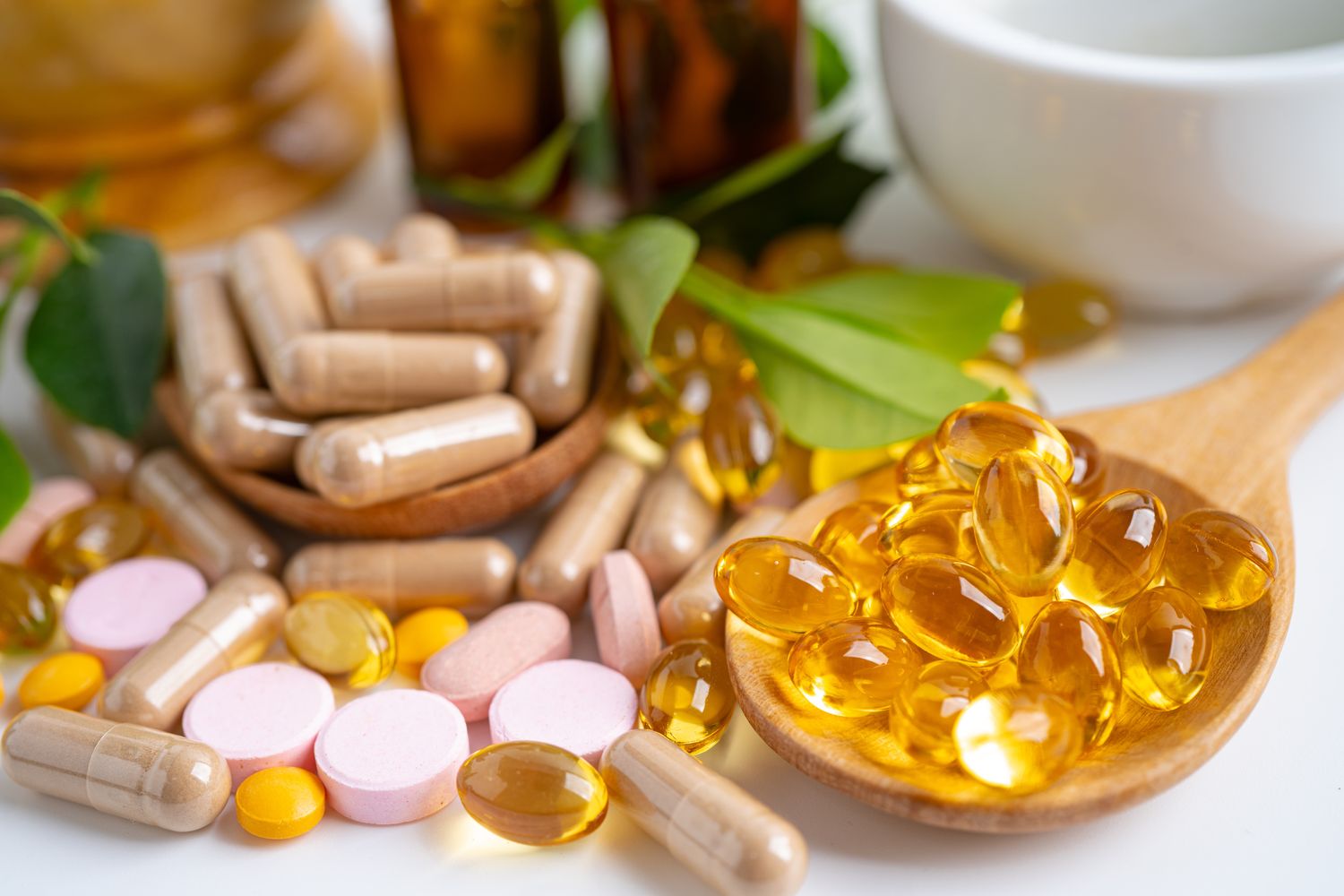 Various types of supplements and vitamins including capsules tablets and gel pills arranged on a table with herbal elements