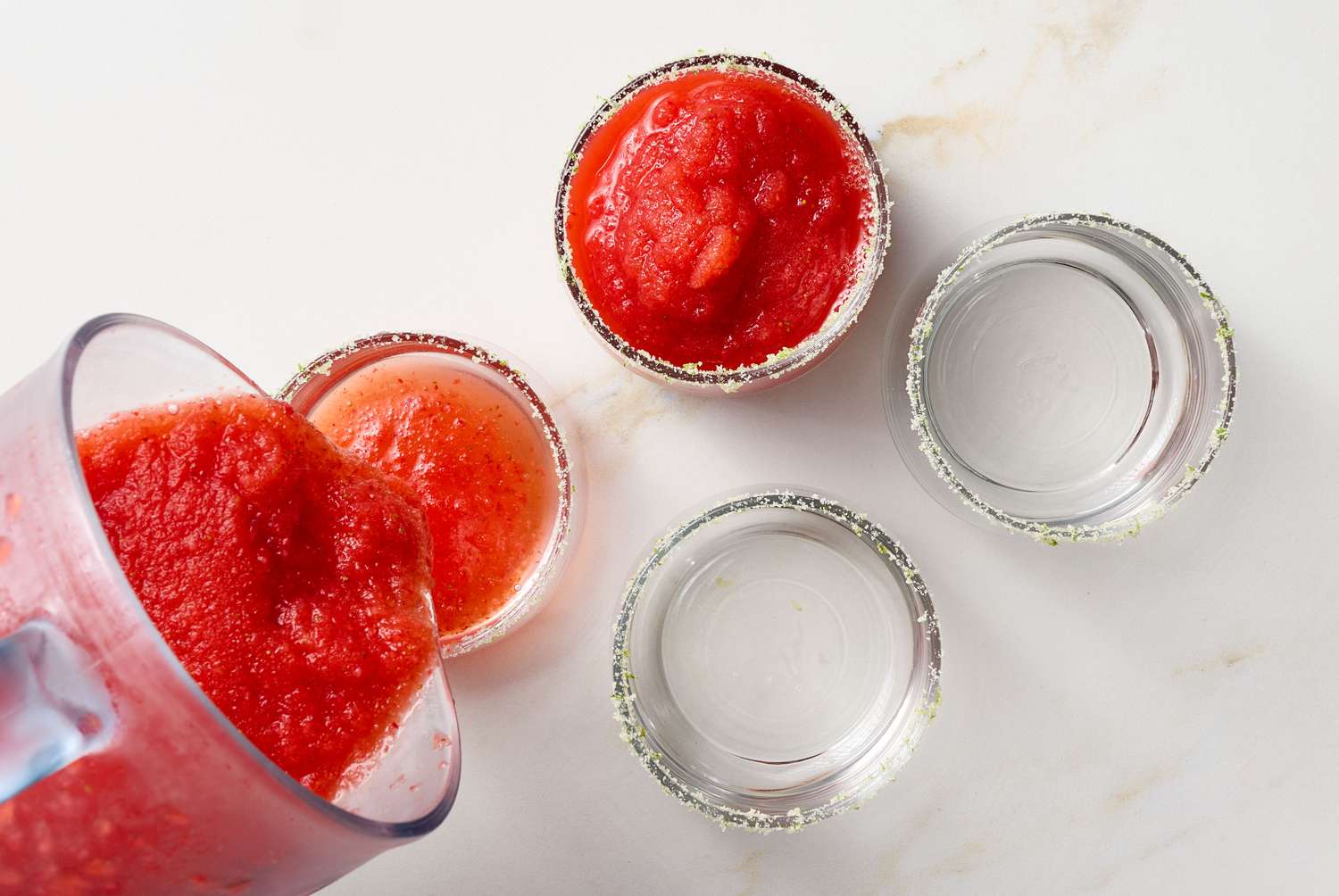 Blended strawberry daiquiri being poured into sugar-rimmed glasses