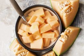 Bowl of cubed cantaloupe with sliced cantaloupe wedges and seeds surrounding