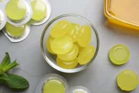 A bowl filled with round medicinal lozenges surrounded by blister packs and mint leaves