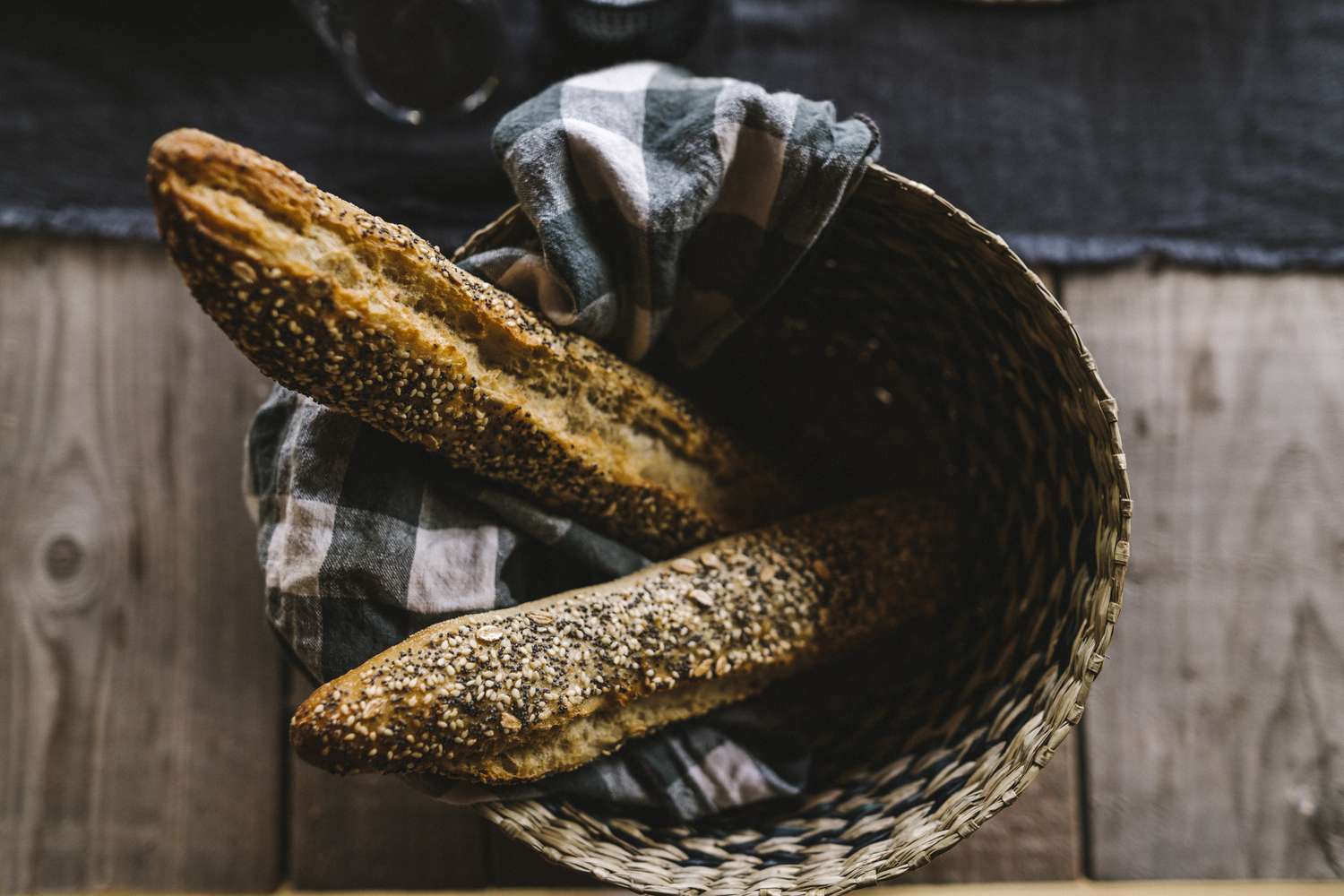 Two baguettes with sesame seeds wrapped in cloth in a basket