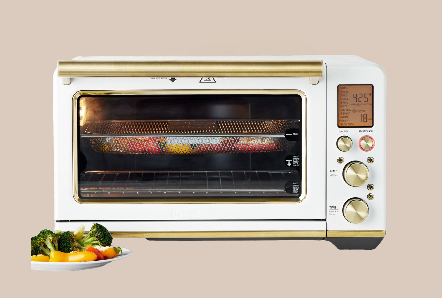 A countertop air fryer with a digital display featuring cooking food inside and a plate of vegetables in the foreground