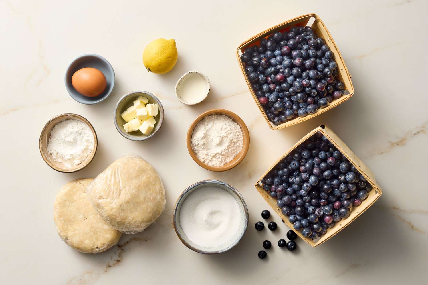 Ingredients for blueberry pie including blueberries, dough, butter, and other components arranged on a surface