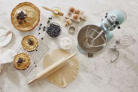 Kitchen setup with a stand mixer baked pies rolling pin and blueberries on a countertop