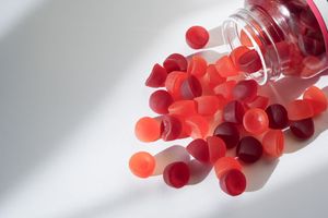 Bottle with red gummy candies spilled on a white surface