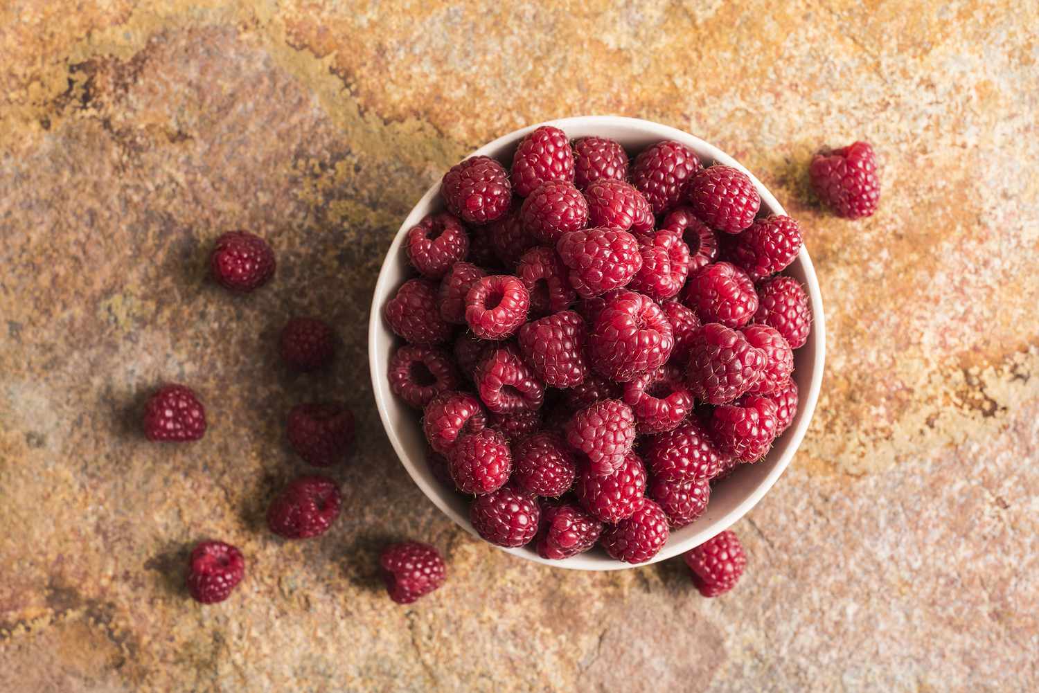 fresh raspberries in a small white bowl and on a surface