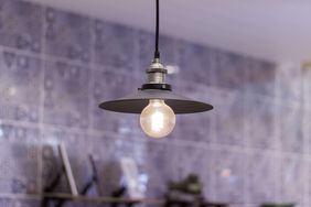 Hanging light fixture with metallic shade and exposed bulb in front of a tiled background