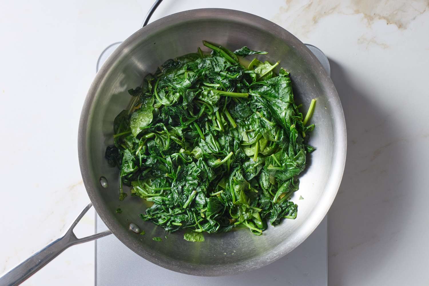 Sauted spinach in a stainless steel frying pan on a stovetop