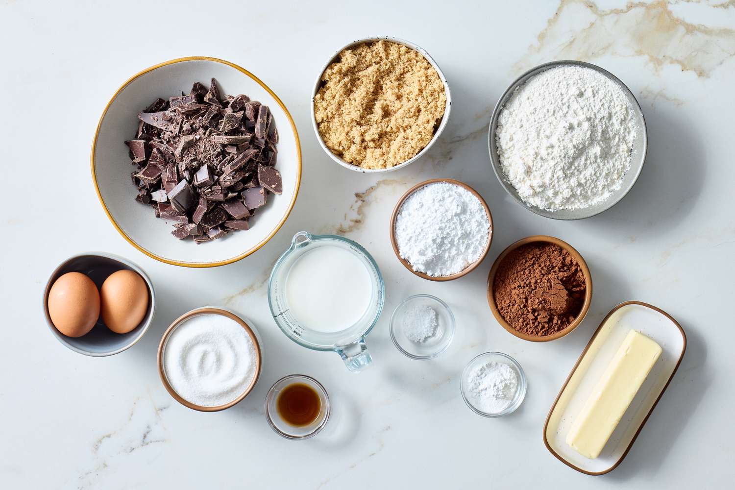 Ingredients for chocolate cookies displayed on a surface including chocolate chunks flour and sugar