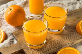 Two glasses of orange juice on a wooden tray with oranges around