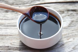 A wooden spoon pouring molasses into a white bowl on a wooden surface