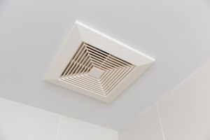 A ceilingmounted ventilation fan with a louvered grille in a room corner