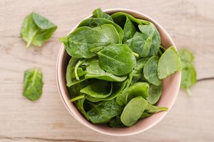 A bowl filled with fresh spinach leaves placed on a wooden surface