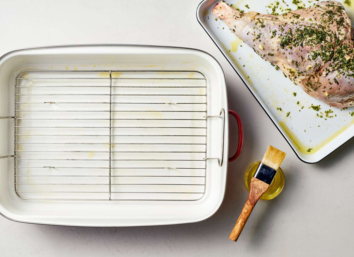 roasting pan and raw leg of lamb with herb mixture and brush
