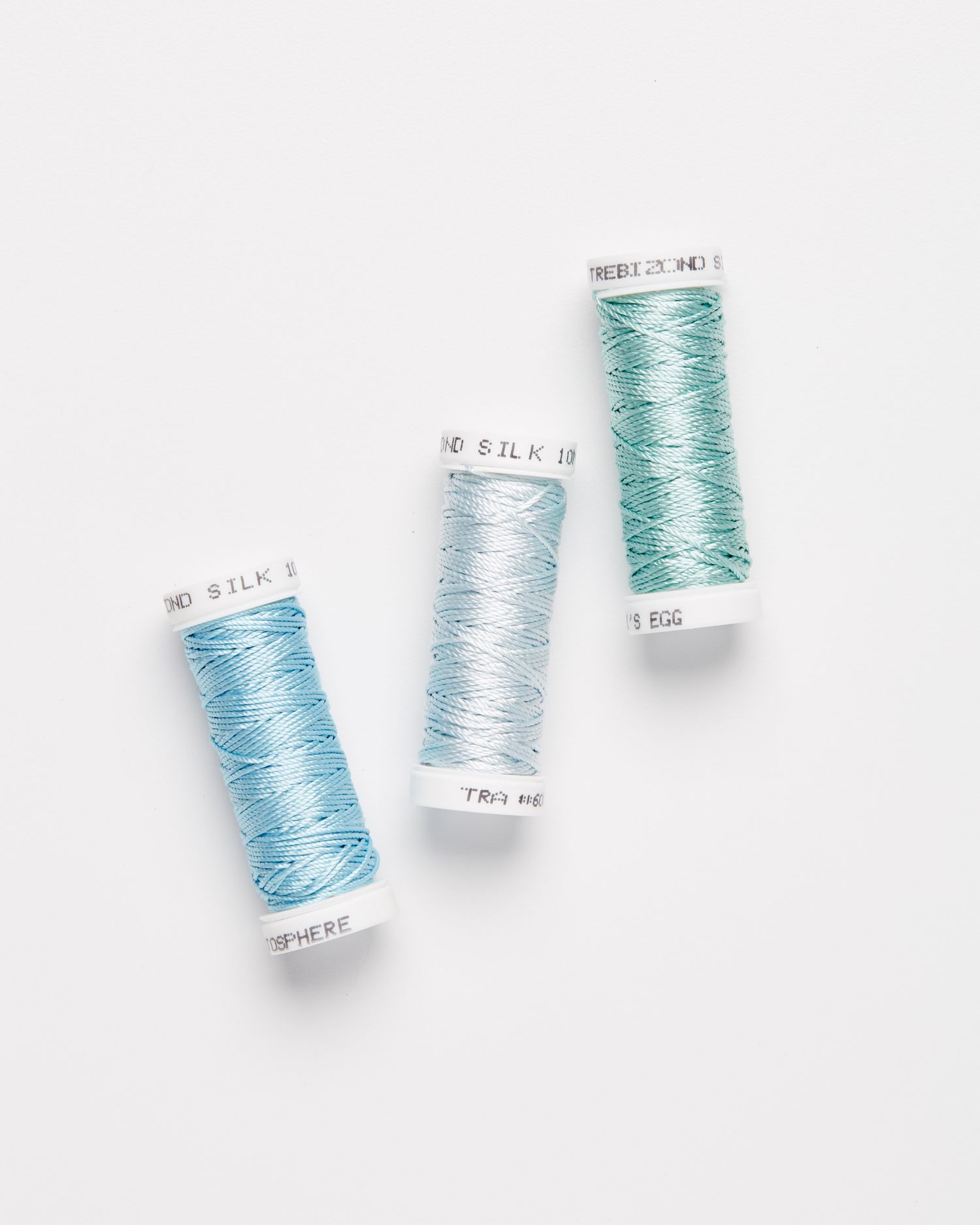three spools of embroidery silk thread against a white background