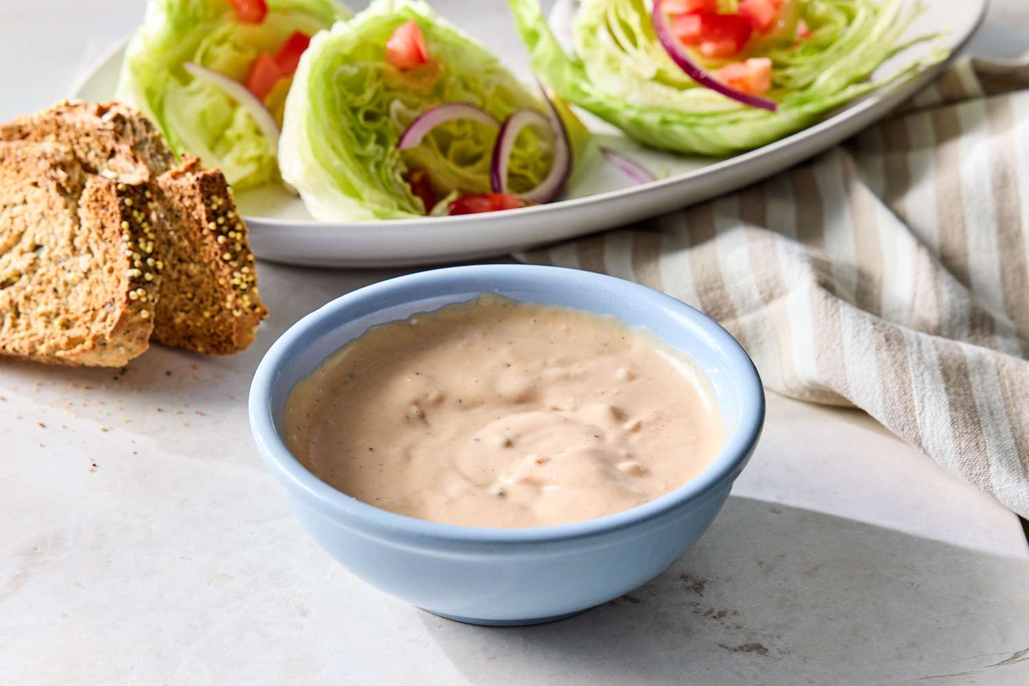 A bowl of Russian dressing with a plate of lettuce wedges and bread slices in the background