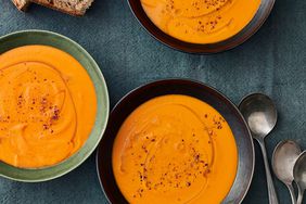 overhead view of bowls of carrot and tomato soup on blue linen