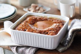 A baked dessert in a square dish on a table with mugs and plates nearby