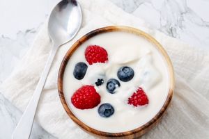 A bowl of yogurt topped with blueberries and raspberries with a spoon on a cloth napkin