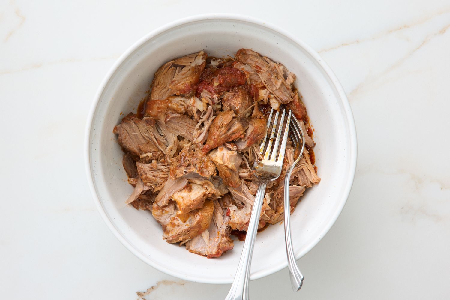 Pulled pork in a white bowl with serving forks