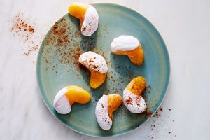 Orange wedges dipped in yogurt and sprinkled with powder arranged on a ceramic plate