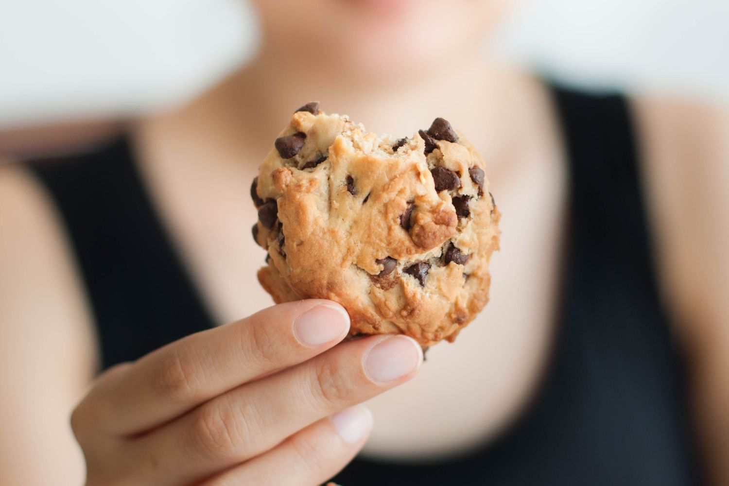 A person holding a partially eaten chocolate chip cookie