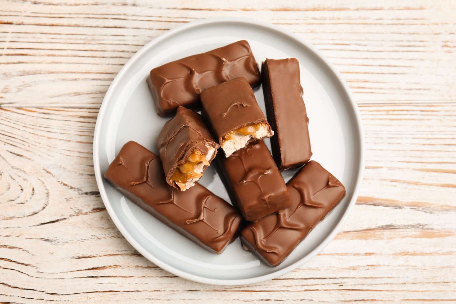 A plate with several chocolate bars including one partially bitten showing caramel and nougat layers on a wooden surface