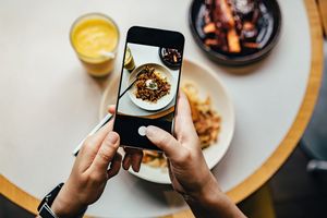 Person taking a photo of a plated dish with a smartphone at a table