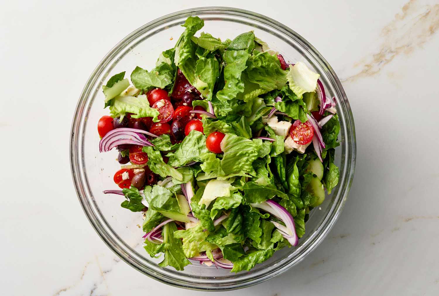 Bowl of Greek salad with mixed greens, cherry tomatoes, red onion, avocado, and other ingredients