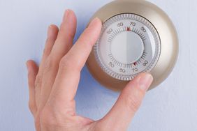 A hand adjusting a round thermostat on a wall