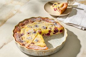 Cherry clafoutis dessert in a baking dish with a slice removed, slice served on a plate with a fork beside it