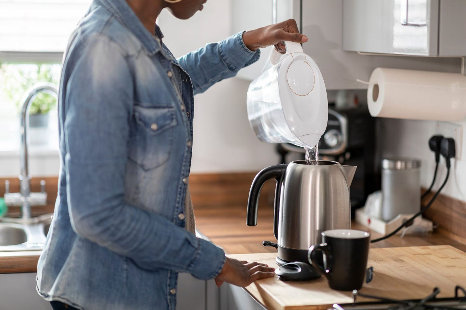 Woman pouring water into kettle in kitchen