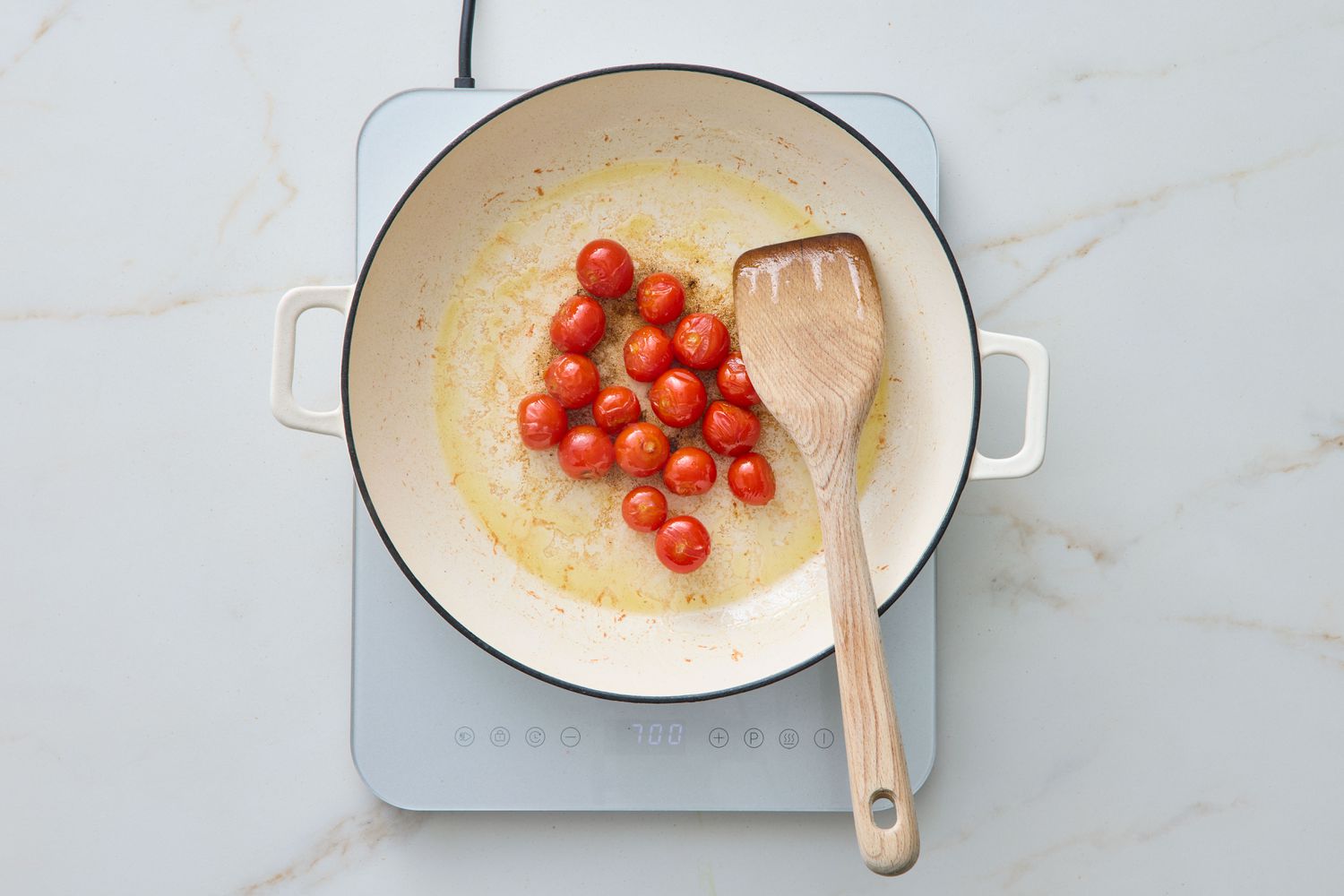 Cherry tomatoes cooking in a pan with a wooden spatula, on an induction cooktop