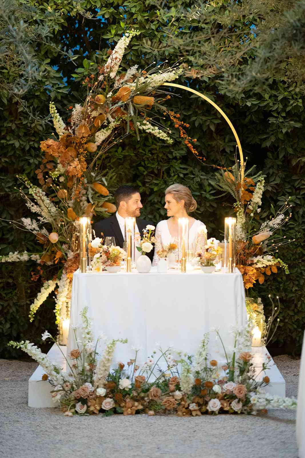 couple sitting at sweet heart table under Ikebana-Style Floral arch