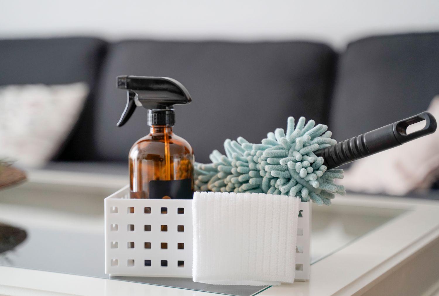 A cleaning kit on a table with a spray bottle a duster and cleaning cloths placed in a small storage container