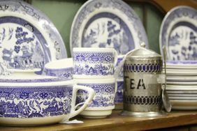 Set of blue patterned porcelain dishes cups and a metal tea container on a wooden shelf