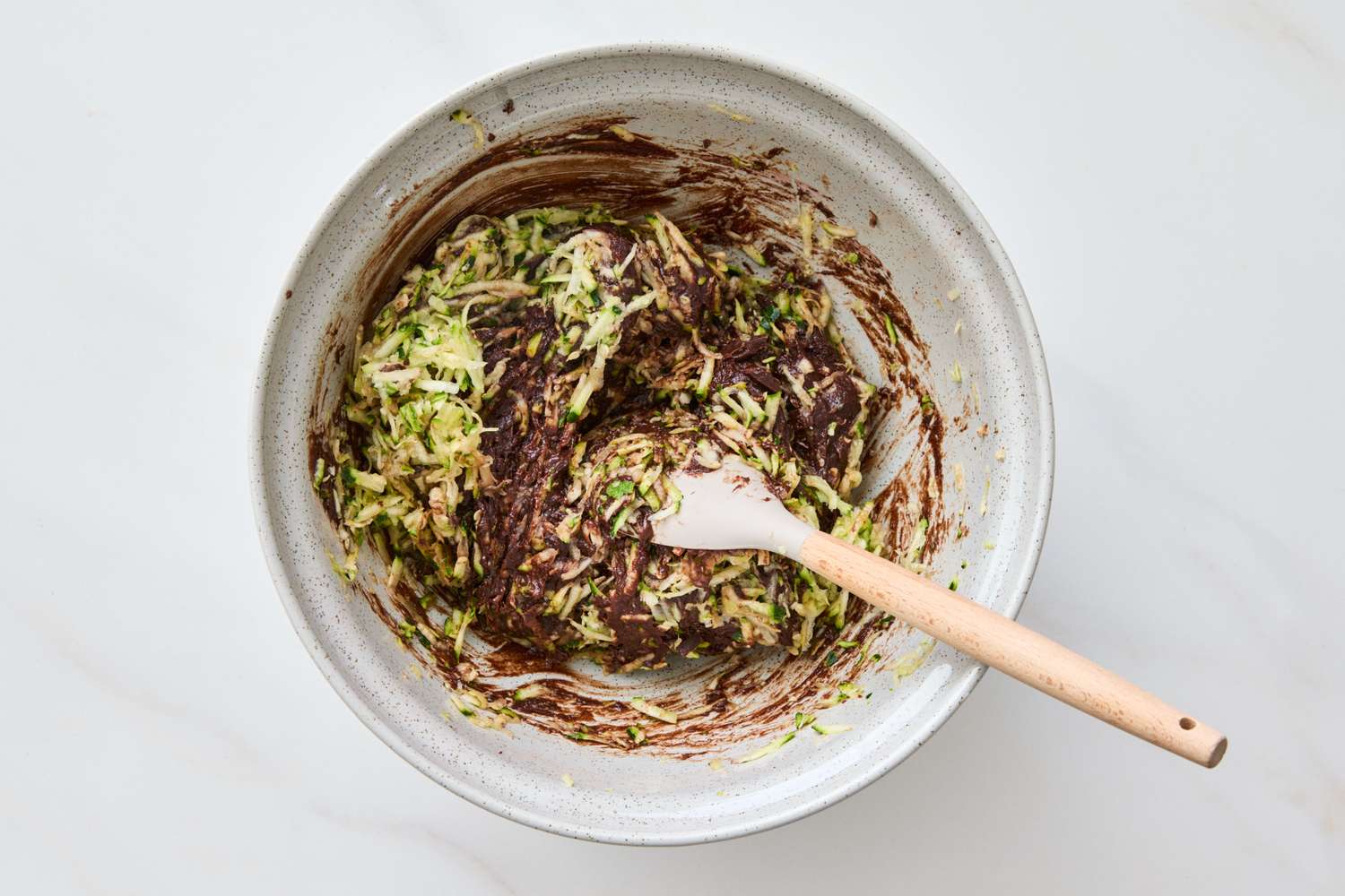 Bowl with mixture of shredded zucchini and chocolate batter white spatula inside