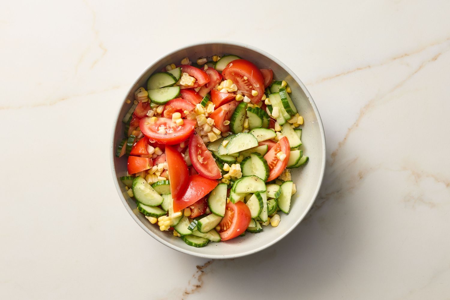A bowl of fresh salad containing sliced tomatoes, cucumbers, and other vegetables