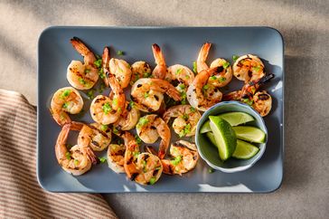 Grilled shrimp on a platter garnished with herbs served with a side of lime wedges