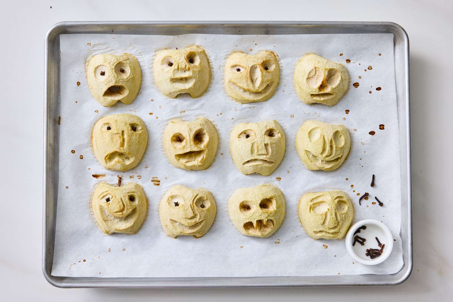 Baking tray with carved apple halves resembling shrunken heads arranged on parchment paper