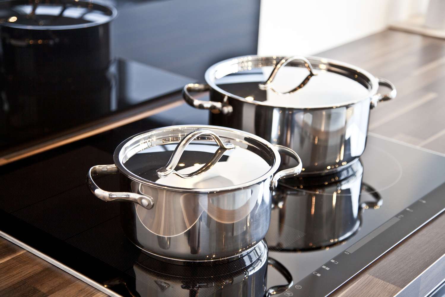 Two stainless steel pots with lids on a modern induction stove
