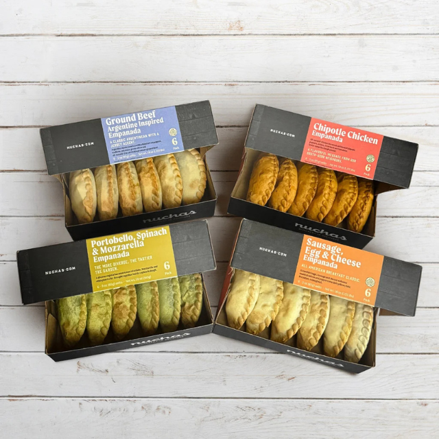 A display of four boxed empanada varieties arranged on a light wooden tabletop