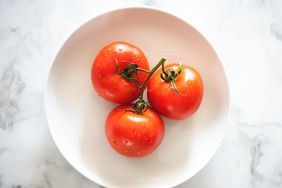 Three ripe red tomatoes on the vine shot in a brightly lit neutral setting.