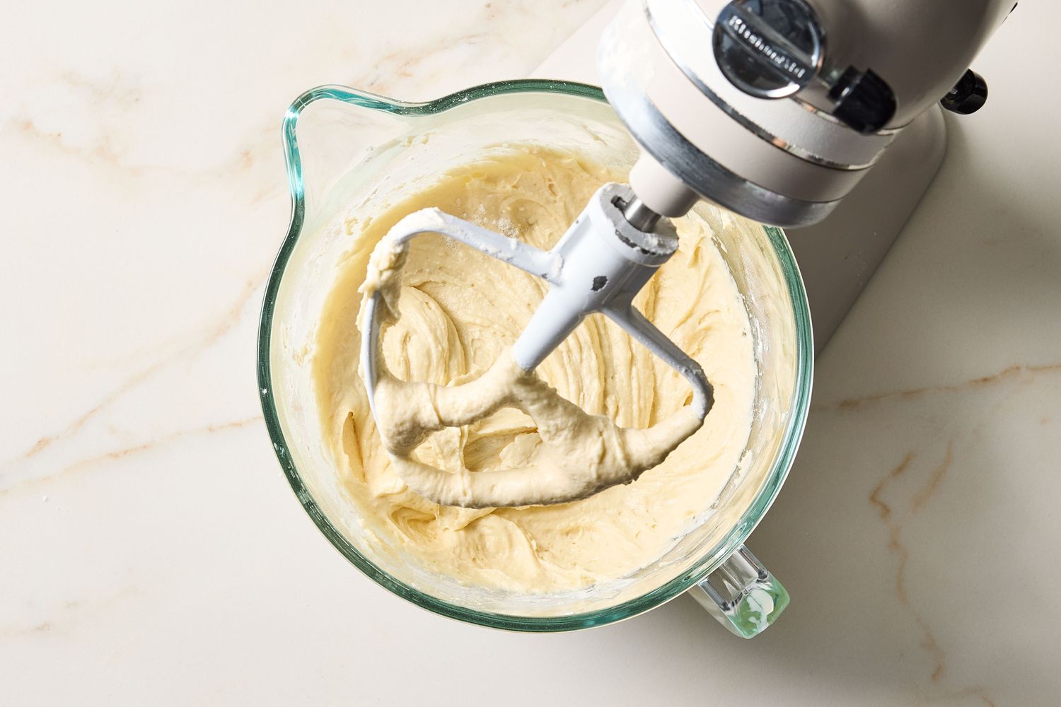A mixer with creamy batter in a glass bowl on a countertop step in a recipe