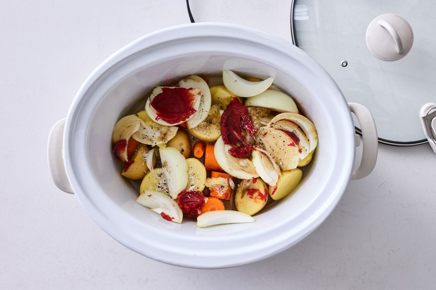 Slow cooker with raw vegetables and sauce prepared for cooking
