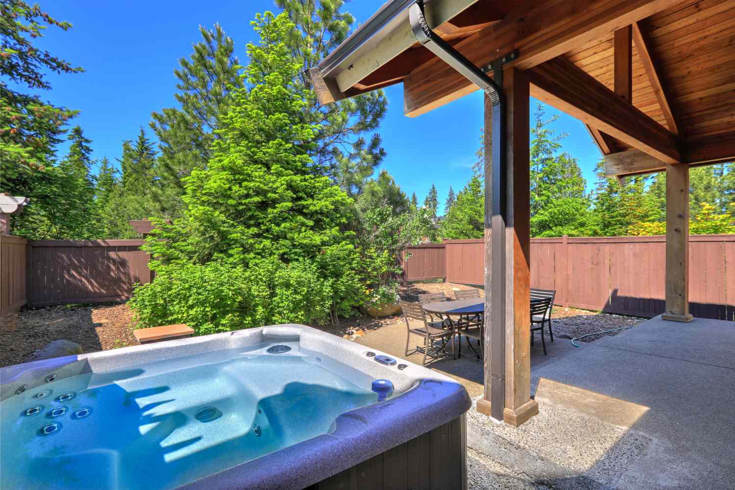 Outdoor hot tub in a backyard next to a covered patio and surrounded by trees