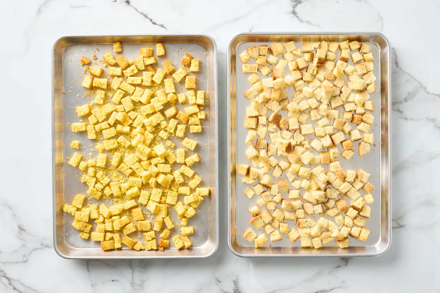 Two baking trays with cubed bread spread evenly
