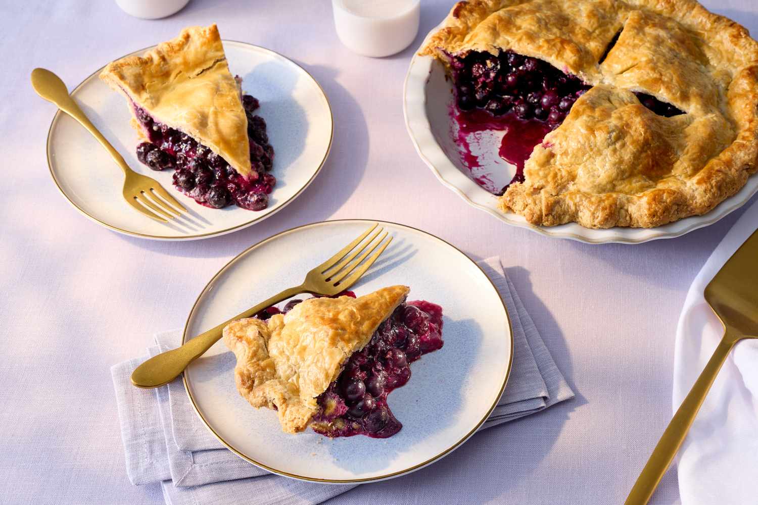 Blueberry pie served with slices on two plates, golden forks placed next to them