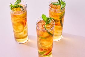 Three glasses of a fruit garnish and herbdecorated beverage on a light background