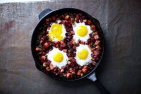 A skillet containing three sunnysideup eggs atop a mixture of diced vegetables and meat